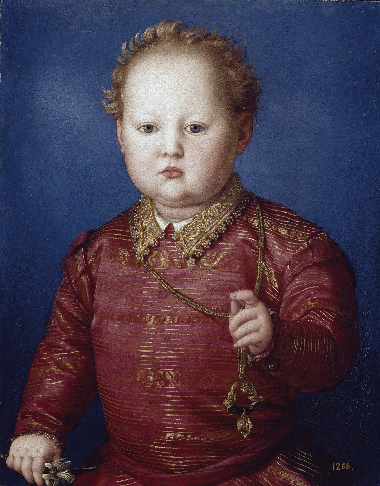 Quadro decorativo de um menino com cabelo encaracolado e bochechas rosadas, vestindo um traje vermelho e dourado, segurando um objeto dourado, sobre um fundo azul escuro. Obra de Agnolo Bronzino.