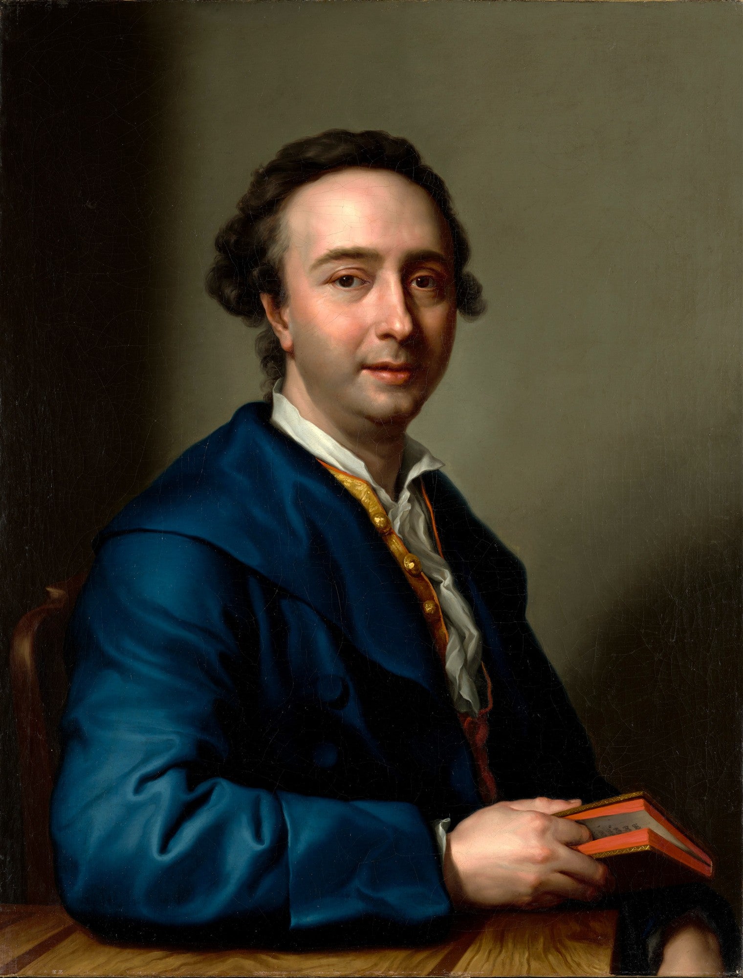 Retrato de Johann Joachim Winckelmann, um homem de meia-idade com cabelo escuro e rosto pálido, vestindo uma túnica azul-marinho e segurando um livro vermelho. Pintura de Anton Raphael Mengs.