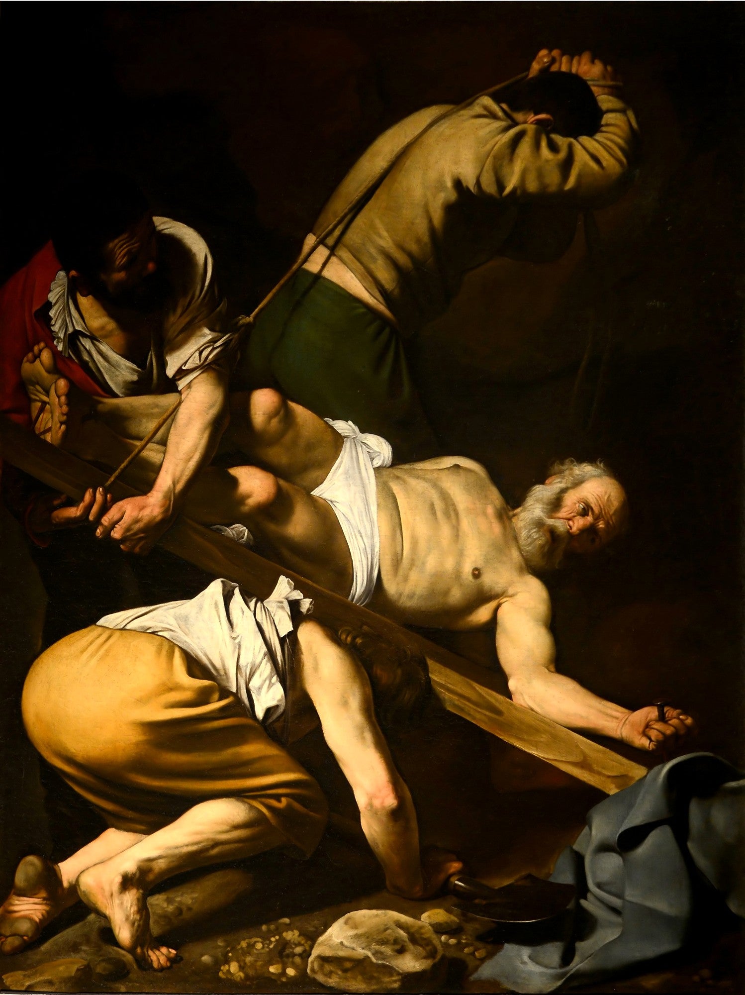 Pintura a óleo de Caravaggio, 'A Crucificação de São Pedro', mostrando três homens crucificando São Pedro de cabeça para baixo, com iluminação dramática e tons terrosos.