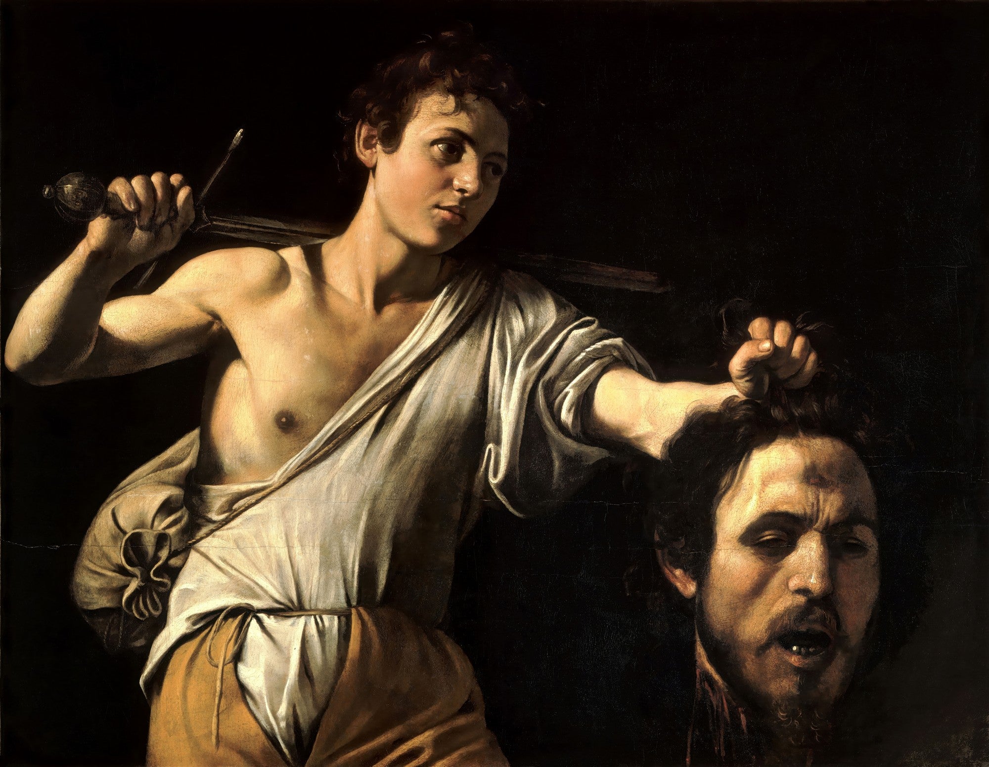 Impressão fine art em papel Kodak de alta qualidade da pintura 'David com a Cabeça de Golias' de Caravaggio. Um jovem Davi, seminu, segura uma espada sobre o ombro e a cabeça decapitada de Golias por seus cabelos, ambos iluminados por uma luz dramática contra um fundo escuro.