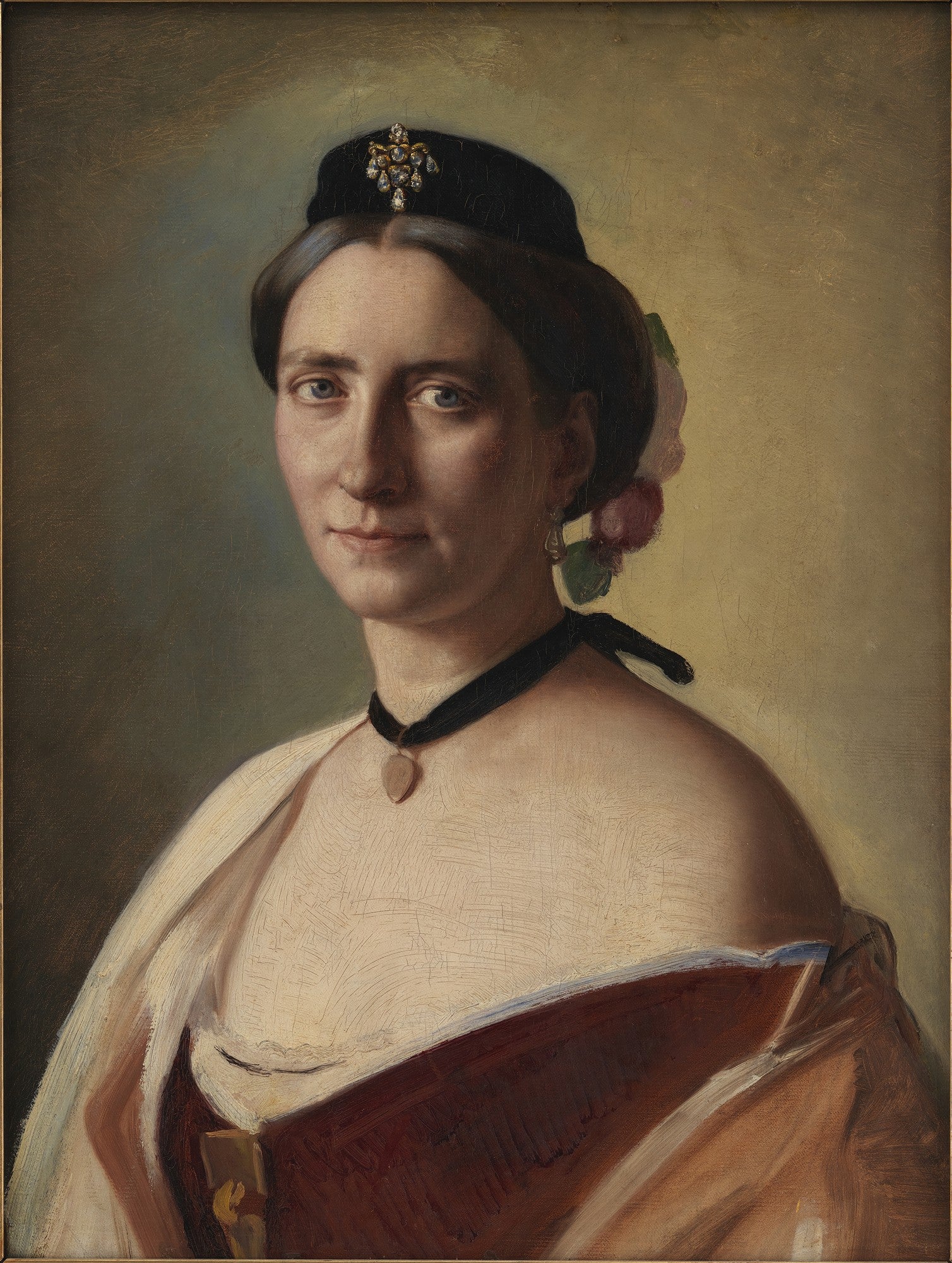 Retrato de uma mulher de meia-idade, com cabelos escuros presos, usando um chapéu preto adornado com joias, um colar de veludo preto com um pingente em forma de coração e brincos delicados. Ela veste um traje que expõe os ombros, com detalhes em tons terrosos. O fundo é neutro e suave, realçando a figura.