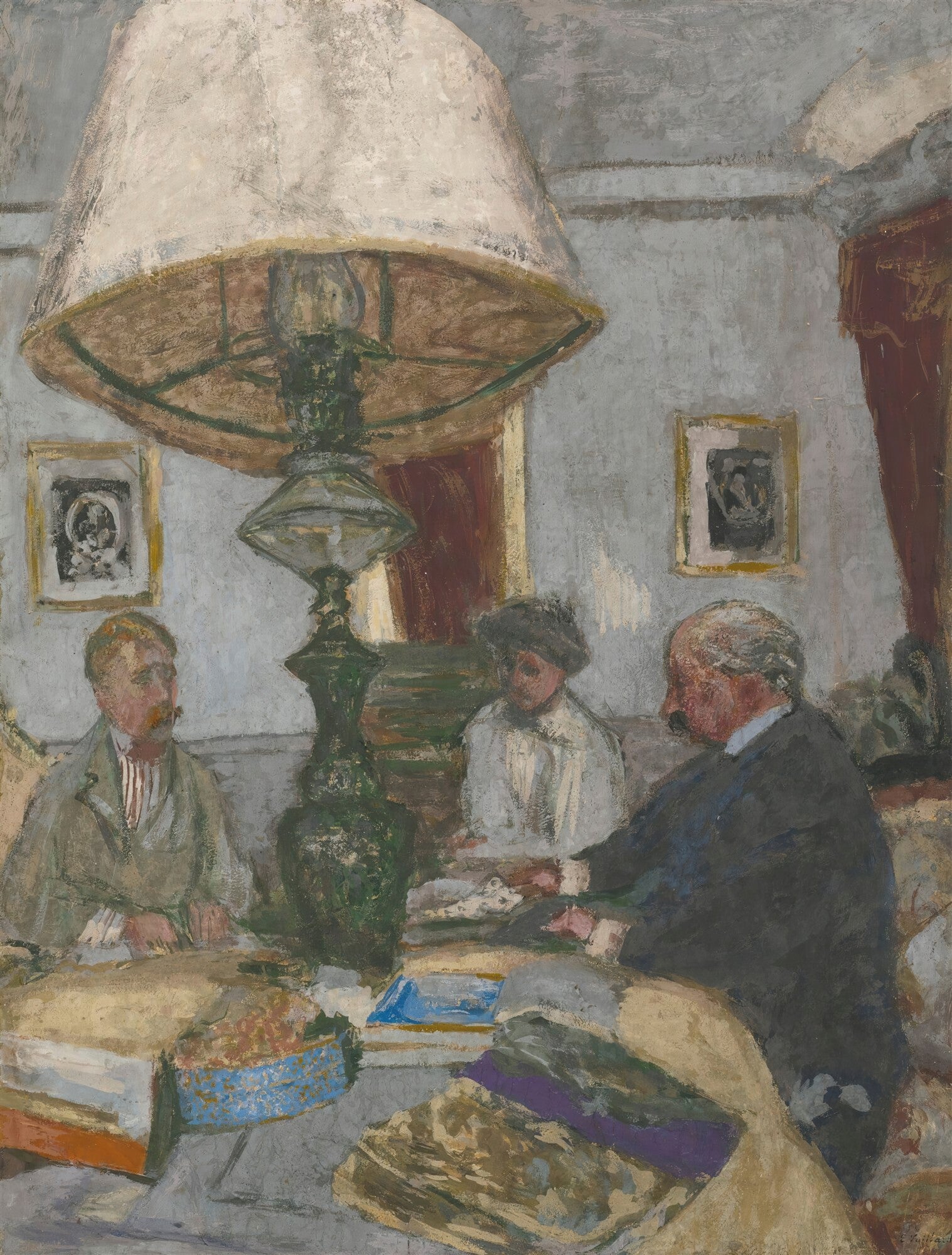 Quadro decorativo "A Mesa de Jantar" de Édouard Vuillard, mostrando três figuras sentadas ao redor de uma mesa iluminada por um grande abajur, em tons de cinza, marrom e verde.