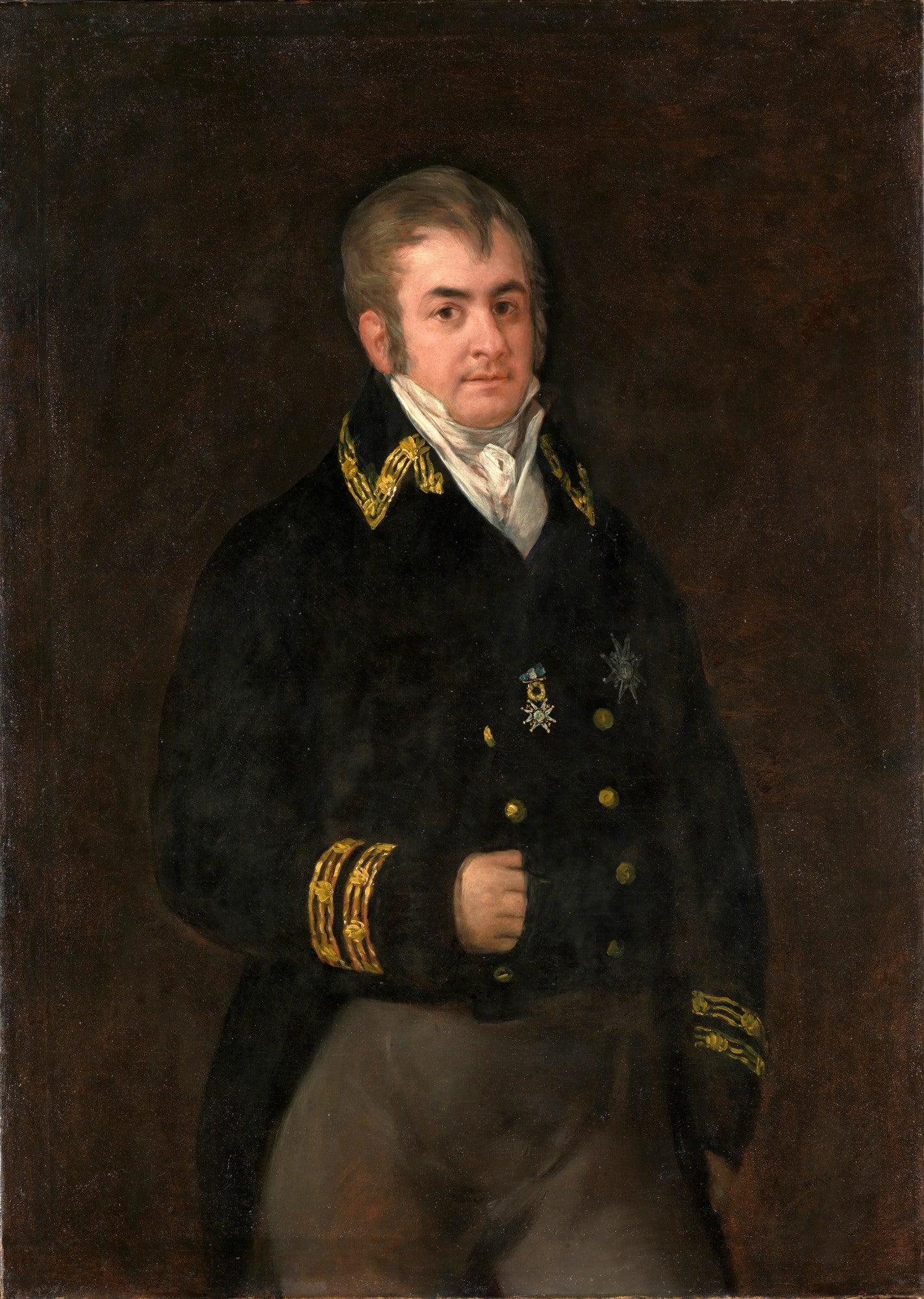 Quadro decorativo com retrato de um oficial masculino, vestido com uniforme militar azul-marinho decorado com detalhes dourados, camisa branca e lenço no pescoço. O fundo é escuro e liso, e o homem tem uma expressão séria e olhar direto. Obra atribuída a Francisco de Goya.
