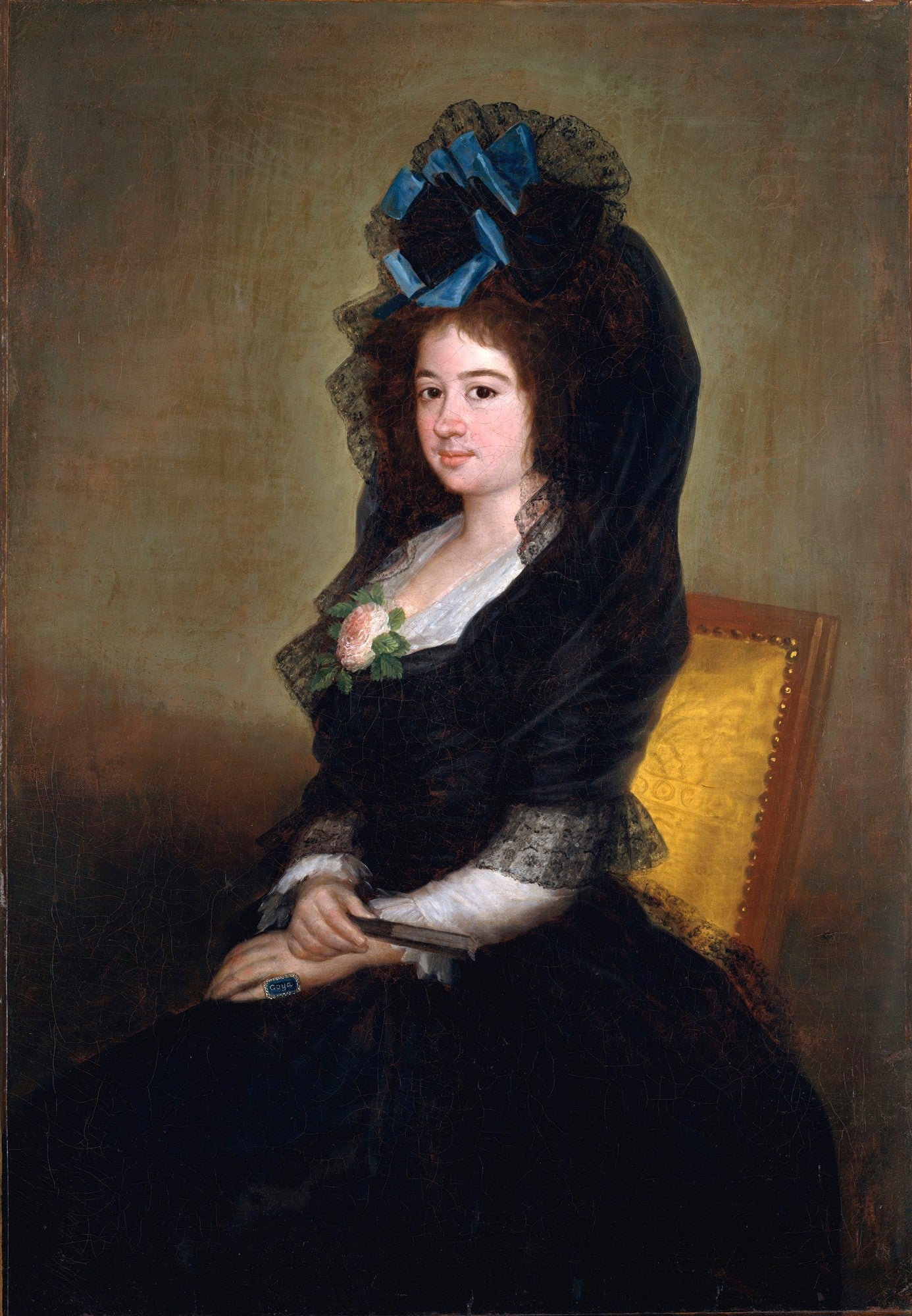 Retrato de uma senhora sentada, com vestes escuras e chapéu com laços azuis, atribuído a Francisco de Goya. A senhora tem pele clara e cabelos escuros, olhando diretamente para frente.