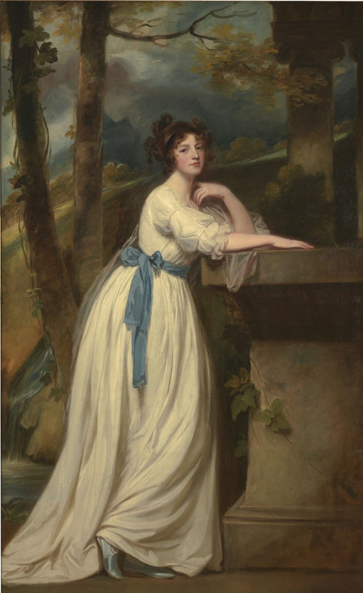 Retrato de corpo inteiro de uma mulher jovem, vestida com um vestido branco esvoaçante e uma faixa azul, apoiada em um pedestal de pedra em um cenário natural com árvores e uma pequena cascata. A mulher tem cabelos castanhos cacheados e um olhar pensativo.