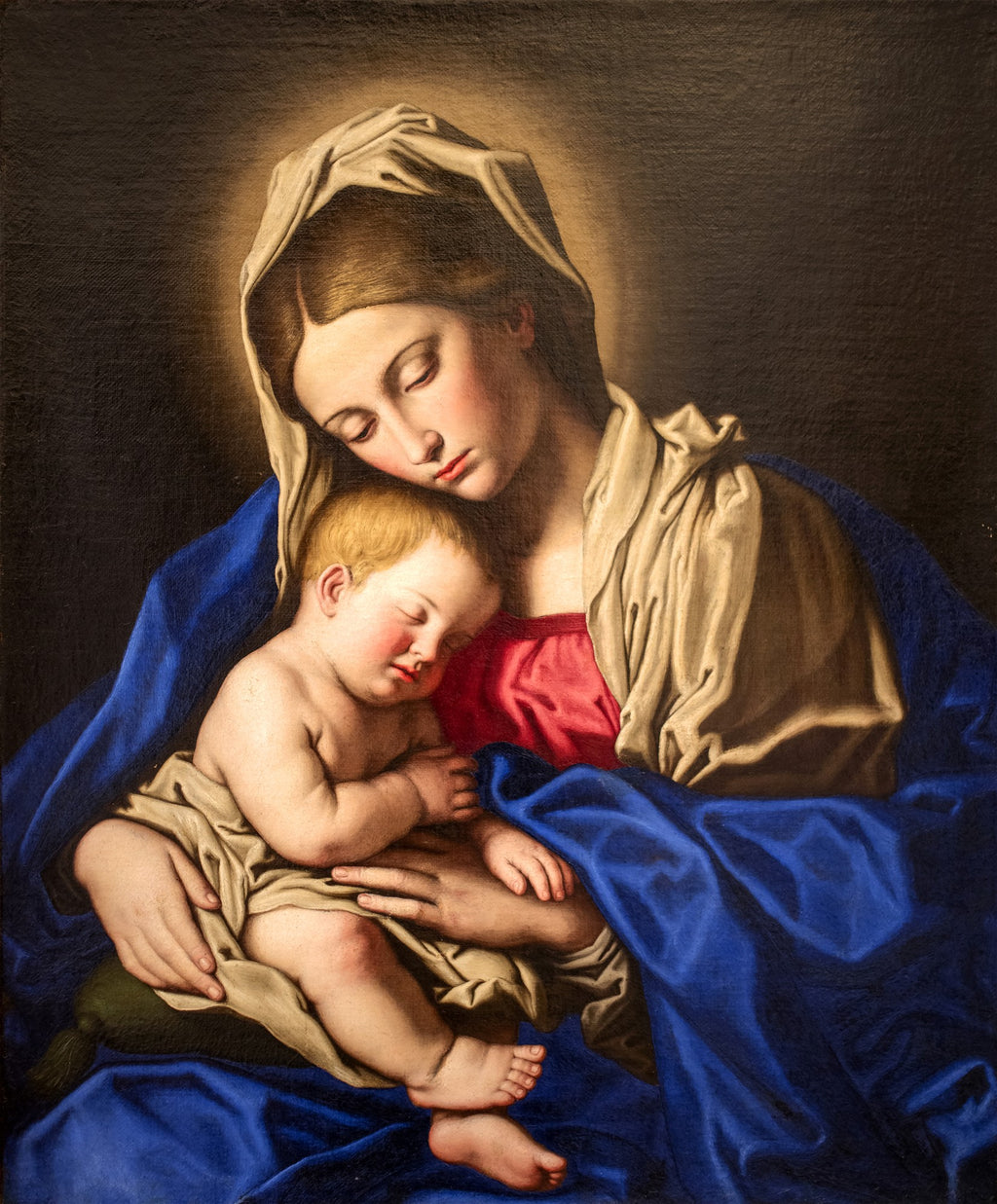 Quadro decorativo da Virgem Maria segurando o Menino Jesus adormecido, pintado por Sassoferrato. A Virgem tem um manto azul vibrante e um vestido vermelho, e o menino está envolto em um tecido claro. A cena é serena e devocional, com um fundo escuro e uma auréola suave.
