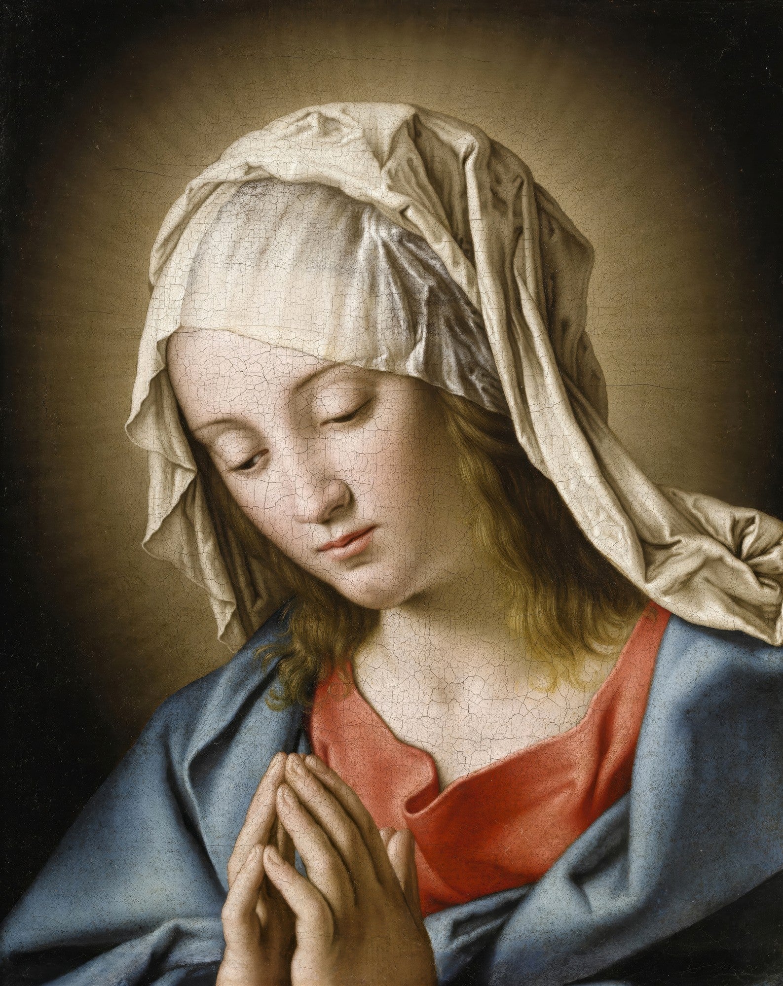 Quadro decorativo da pintura 'A Virgem em Oração' de Sassoferrato, mostrando o rosto sereno de uma mulher com véu branco, vestes azuis e vermelhas, e mãos unidas em prece, com fundo escuro. A imagem apresenta textura de craquelê na superfície.