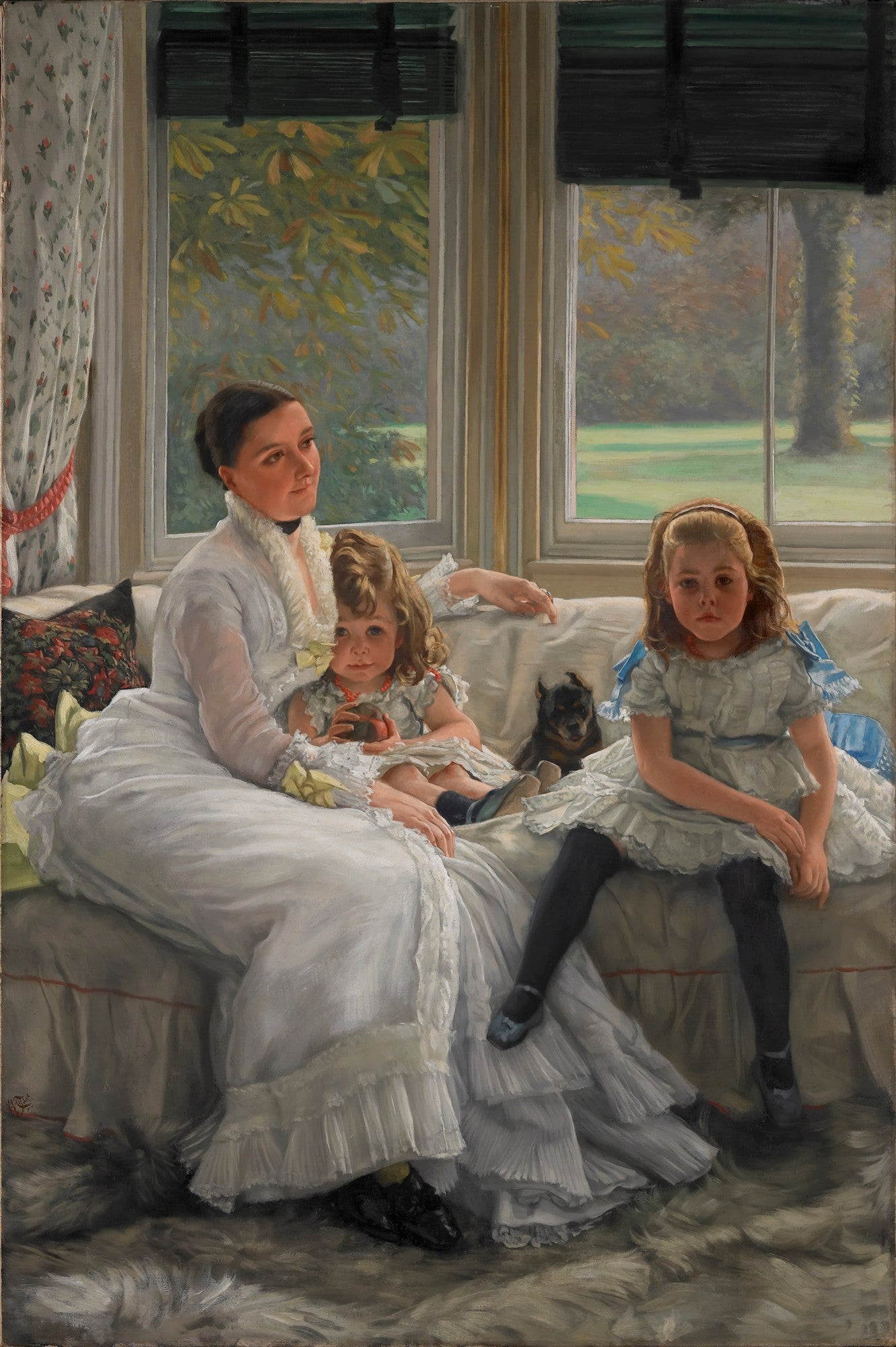 Quadro decorativo mostrando uma mulher sentada em um sofá branco, segurando uma criança pequena no colo, enquanto outra criança está sentada ao lado. Há um pequeno cachorro preto entre as crianças. Ao fundo, uma janela grande revela uma paisagem verde com árvores.