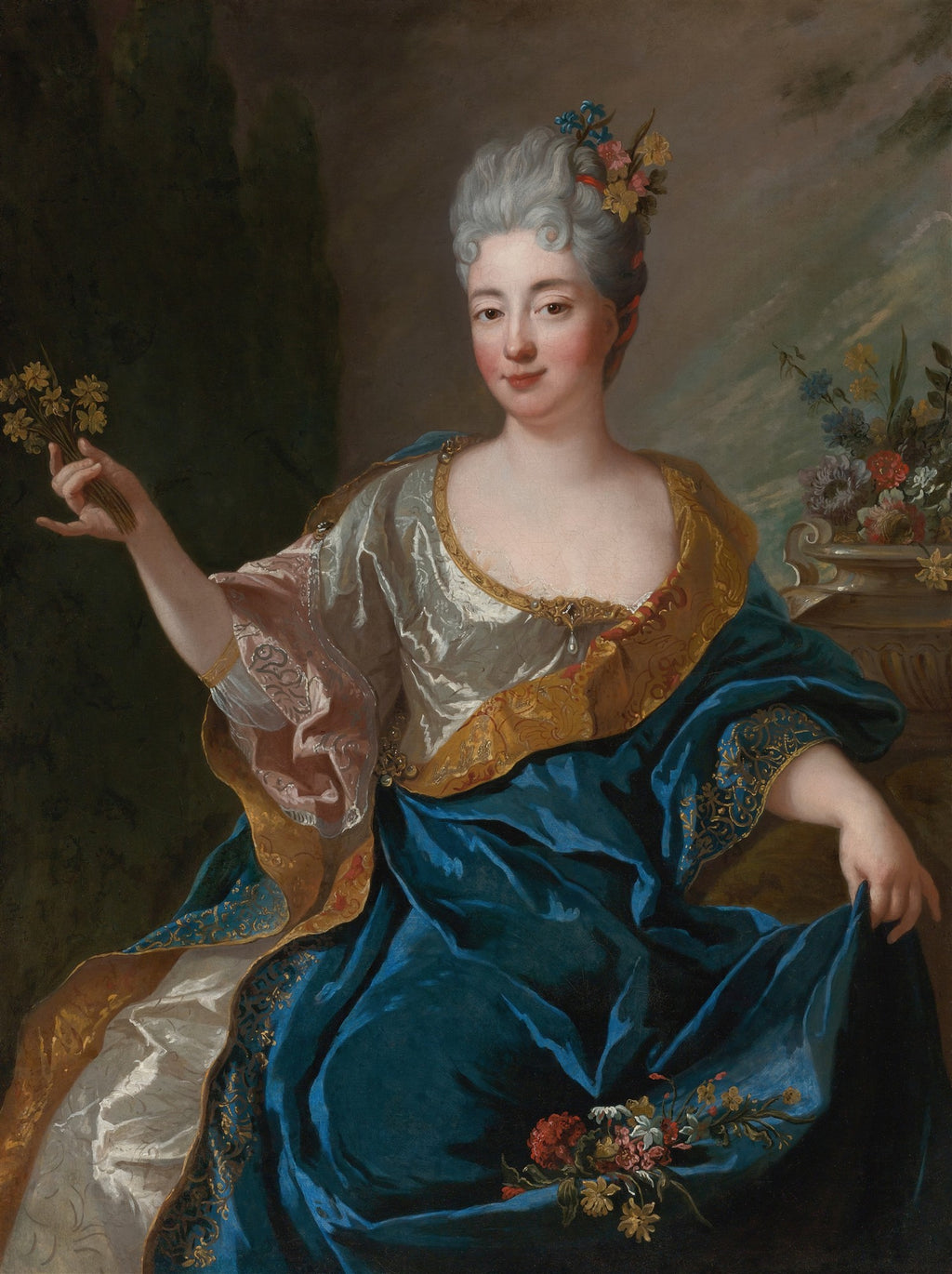 Retrato de uma dama do século XVIII, com cabelos grisalhos e flores coloridas na cabeça, segurando um pequeno buquê de flores amarelas. Ela veste um vestido suntuoso em tons de azul, dourado e rosa pálido, com detalhes ricos. O fundo é escuro, com um toque de paisagem esmaecida à direita, onde há um vaso com mais flores.