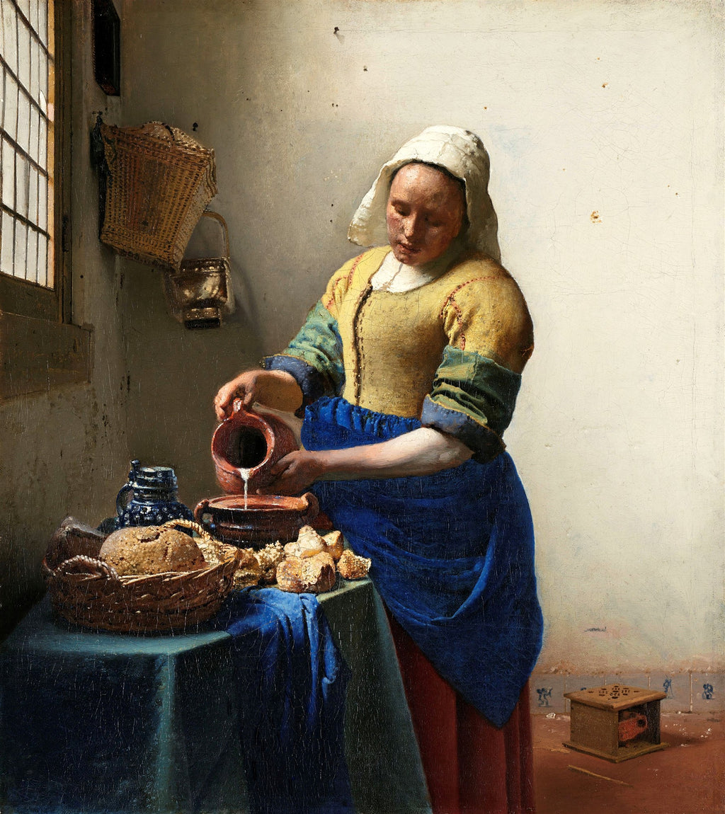Uma mulher vestida com roupas de época, derramando leite de uma jarra para uma tigela sobre uma mesa com pães e cestas, em uma cena de interior iluminada por uma janela. Obra 'A Leiteira' de Johannes Vermeer.