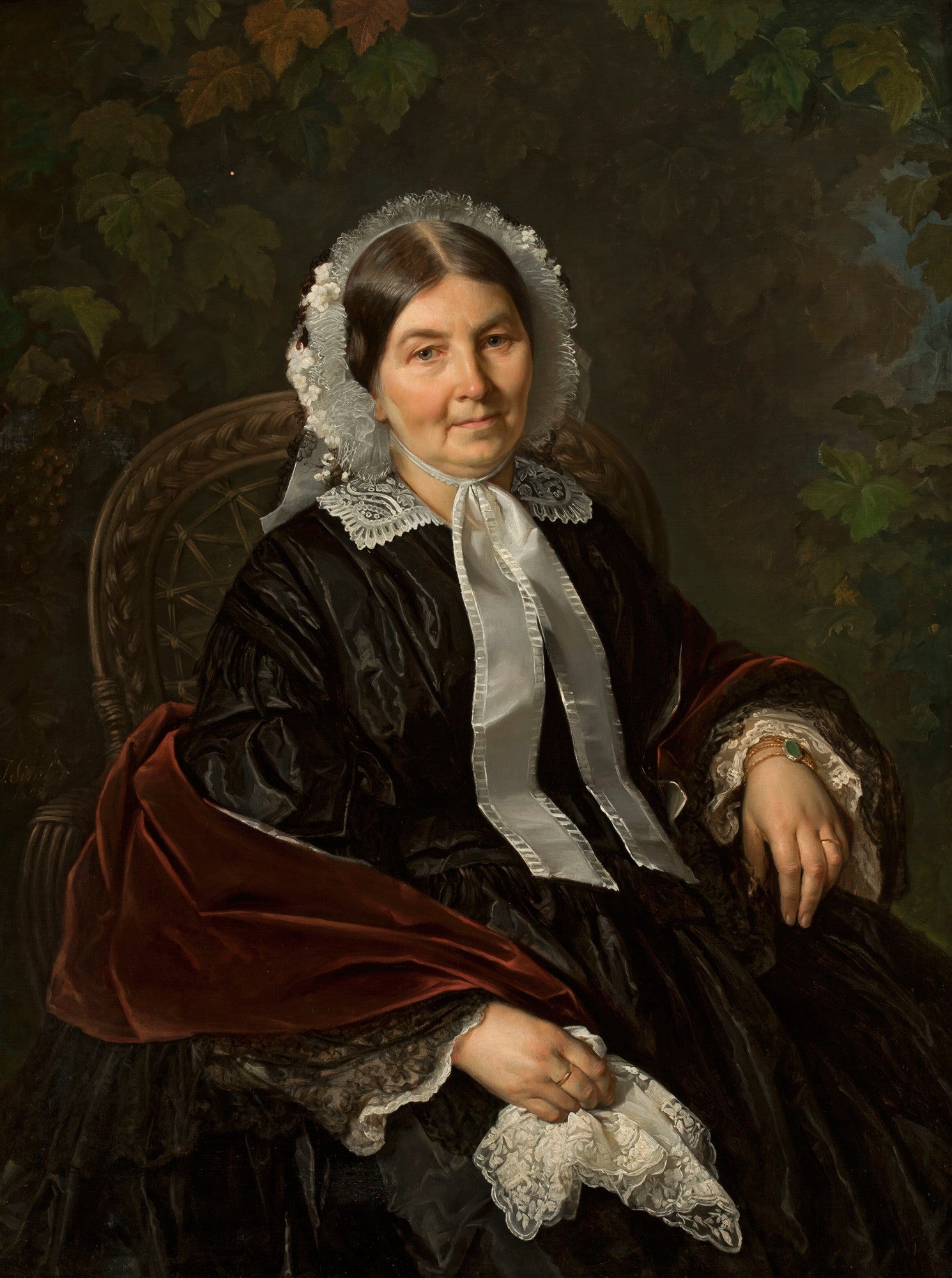 Retrato de uma mulher sentada, de meia-idade, com um lenço de cabeça branco rendado e um vestido escuro com detalhes em renda e veludo vermelho. O fundo é escuro com folhagens verdes e marrons. A mulher segura um lenço de renda nas mãos.