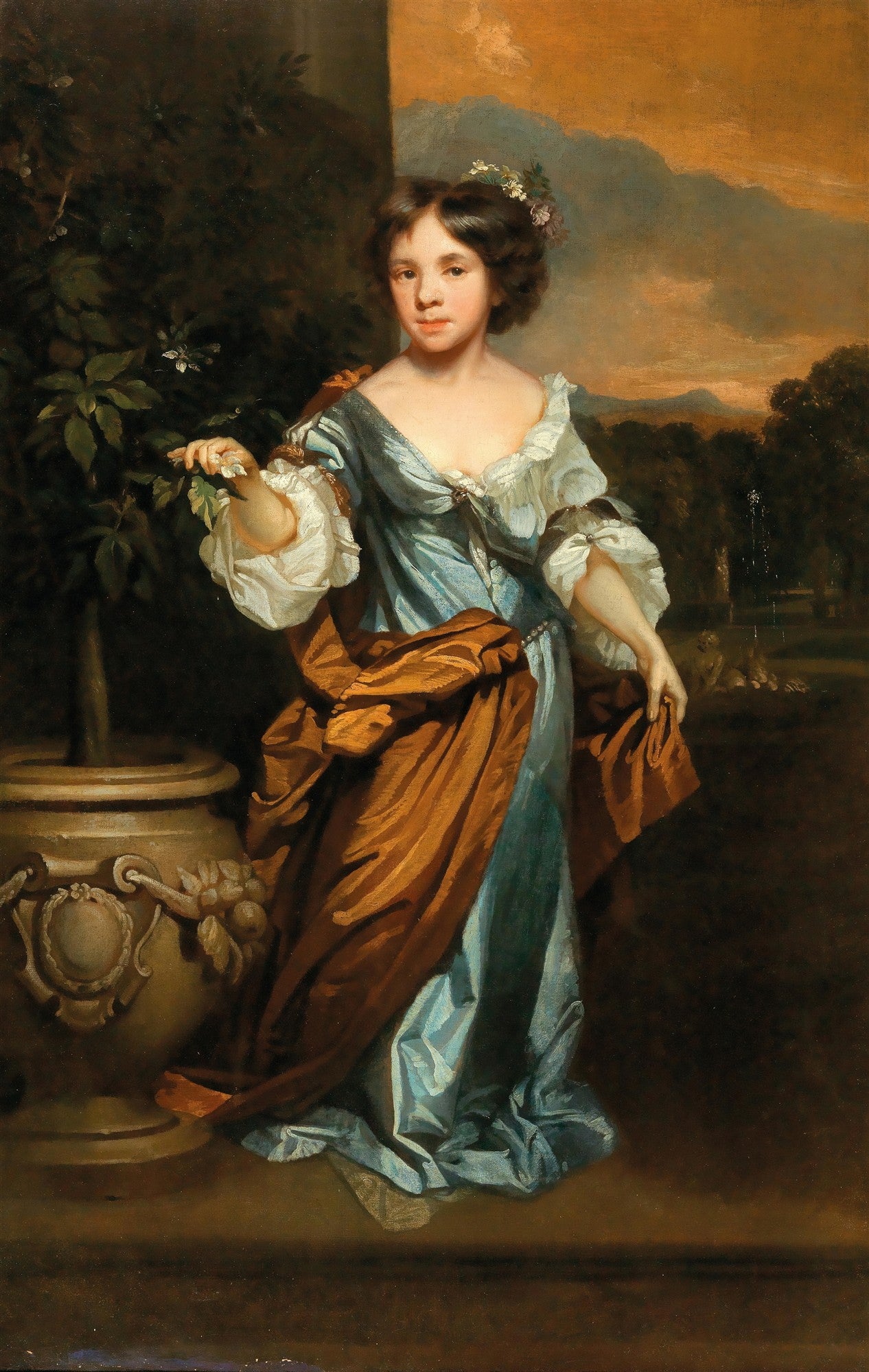 Retrato de uma jovem com cabelos escuros, vestindo um elegante vestido azul e branco, segurando folhas de uma pequena laranjeira em um vaso ornamentado. Ao fundo, uma paisagem com montanhas e céu alaranjado. Obra de Nicolaes Maes.