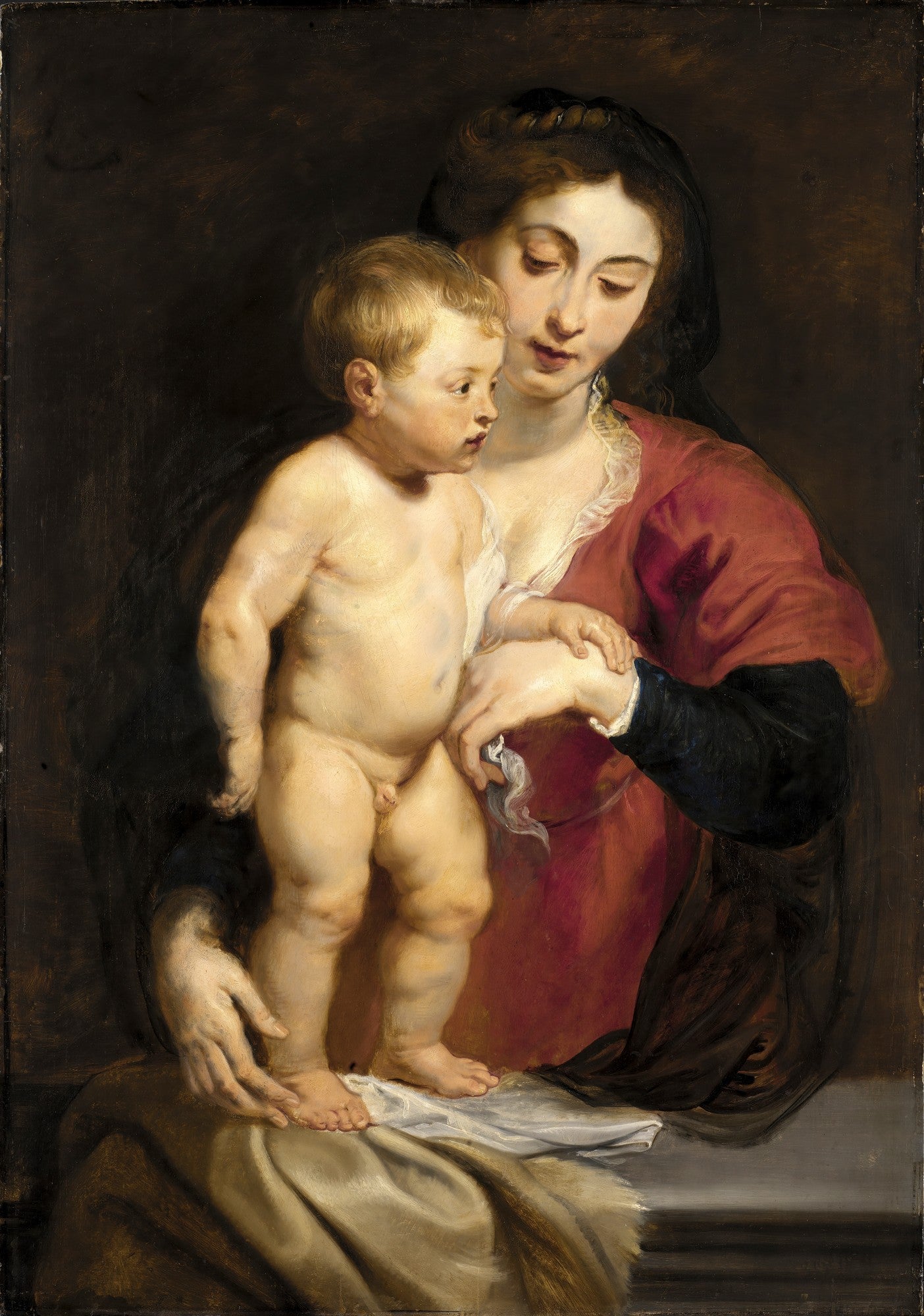 Quadro decorativo com pintura da Virgem Maria segurando o Menino Jesus. A Virgem tem um vestido vermelho e uma expressão carinhosa. O Menino Jesus está nu, com cabelos loiros e pele rosada. A iluminação é dramática, com fundo escuro. Obra atribuída a Peter Paul Rubens.
