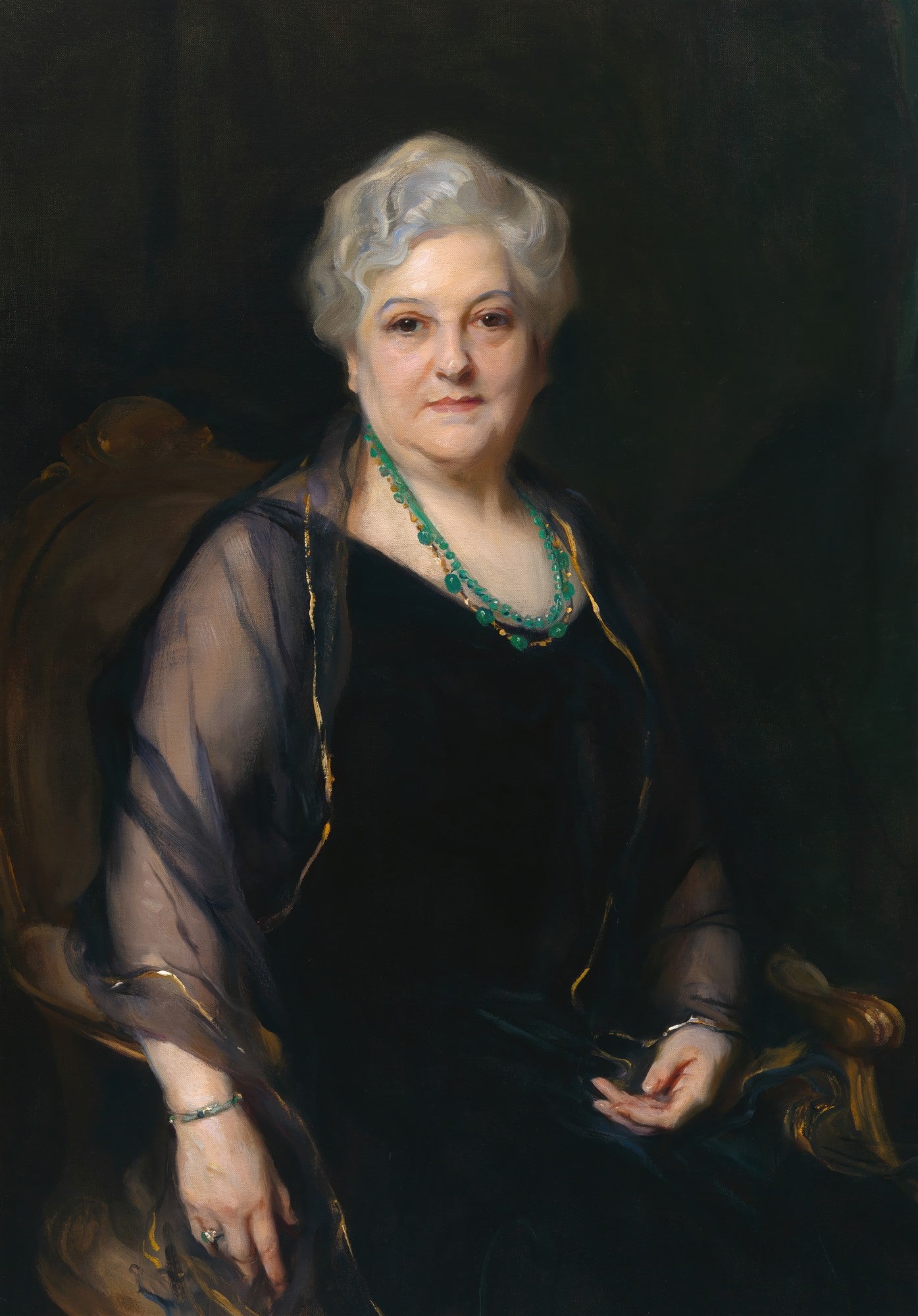 Retrato de uma senhora idosa com cabelos grisalhos, vestindo um vestido preto e um xale transparente, adornada com um colar de esmeraldas, sentada em uma cadeira elegante. O fundo é escuro.