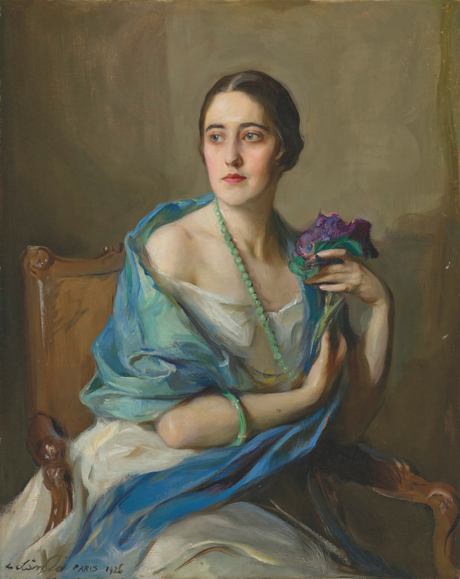 Retrato de uma mulher jovem e elegante, com cabelo escuro, usando um colar de contas verdes e um xale azul sobre um vestido branco, segurando flores violetas, sentada em uma cadeira de madeira, pintada por Philip Alexius de László.
