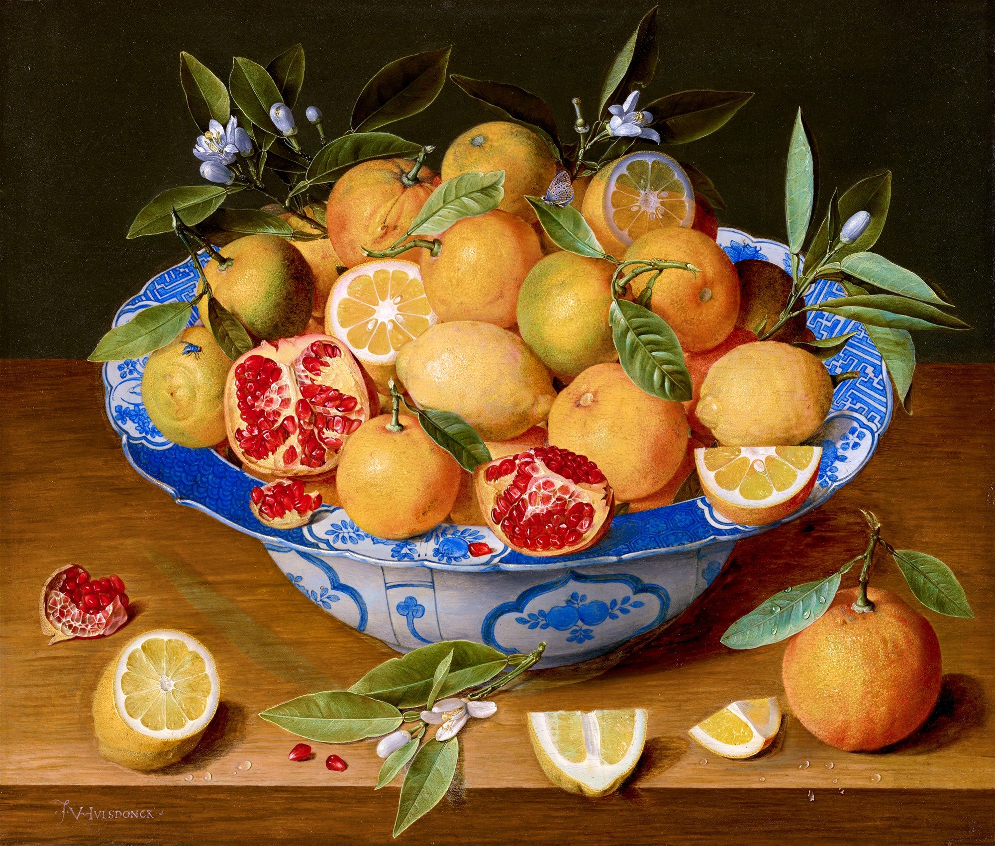 Cesto de frutas cítricas e romãs em uma tigela de porcelana azul e branca sobre uma mesa de madeira. Limões, laranjas e romãs abertas com sementes vermelhas são visíveis, com folhas verdes e flores brancas. A assinatura 'F. I. van Velde' está no canto inferior esquerdo.