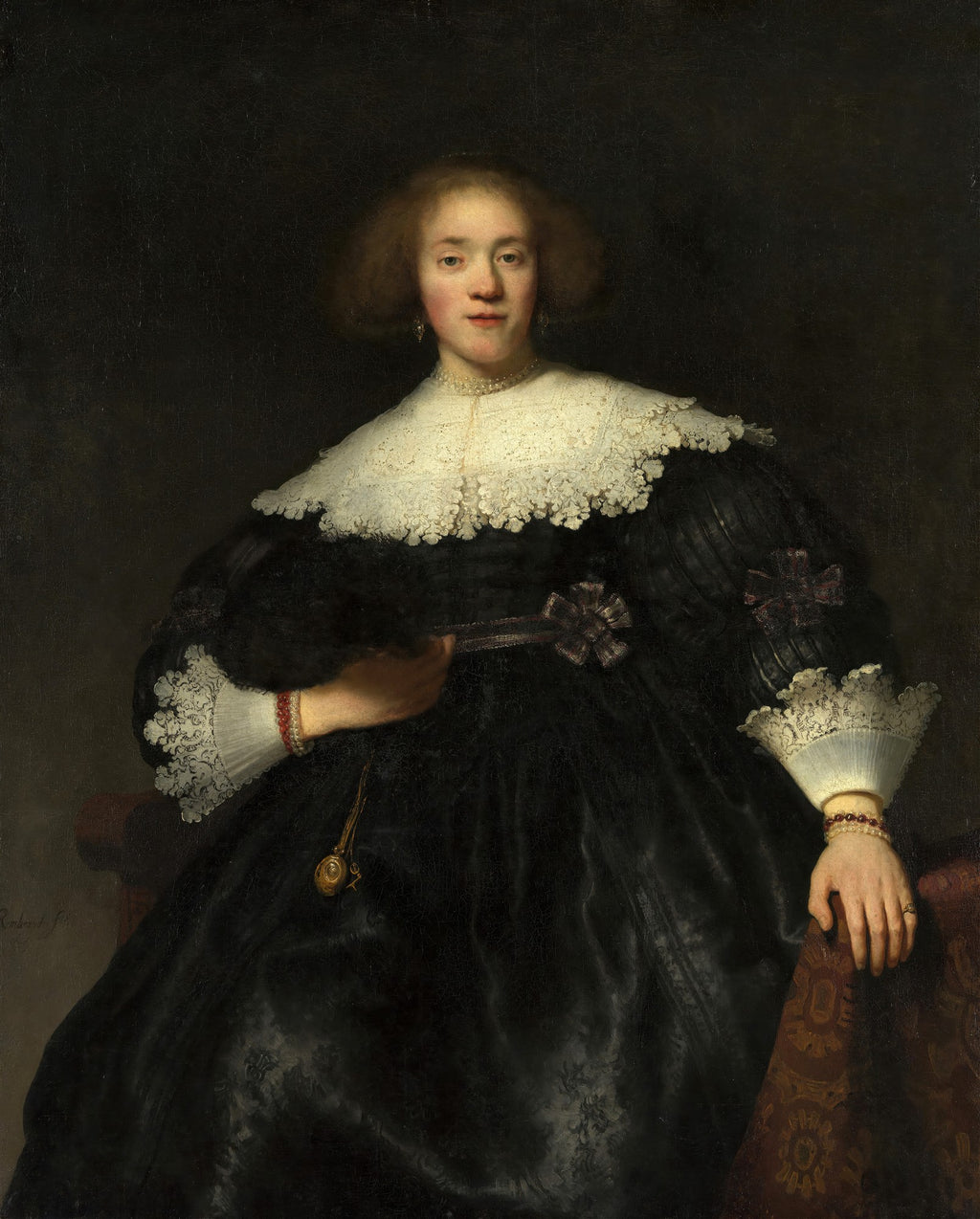 Retrato de uma mulher jovem com cabelo ruivo e encaracolado, vestindo um vestido preto com gola de renda branca e mangas detalhadas, segurando um objeto na mão. A iluminação destaca o rosto e a gola contra um fundo escuro. Obra de Rembrandt.