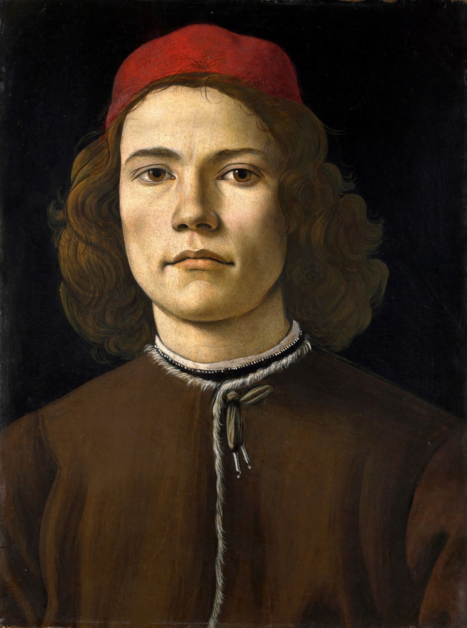 Retrato de um jovem renascentista, possivelmente Giuliano de Medici, pintado por Sandro Botticelli. O jovem tem cabelos castanhos ondulados, um chapéu vermelho e veste uma túnica marrom. O fundo é escuro. A imagem destaca a serenidade e a técnica artística.