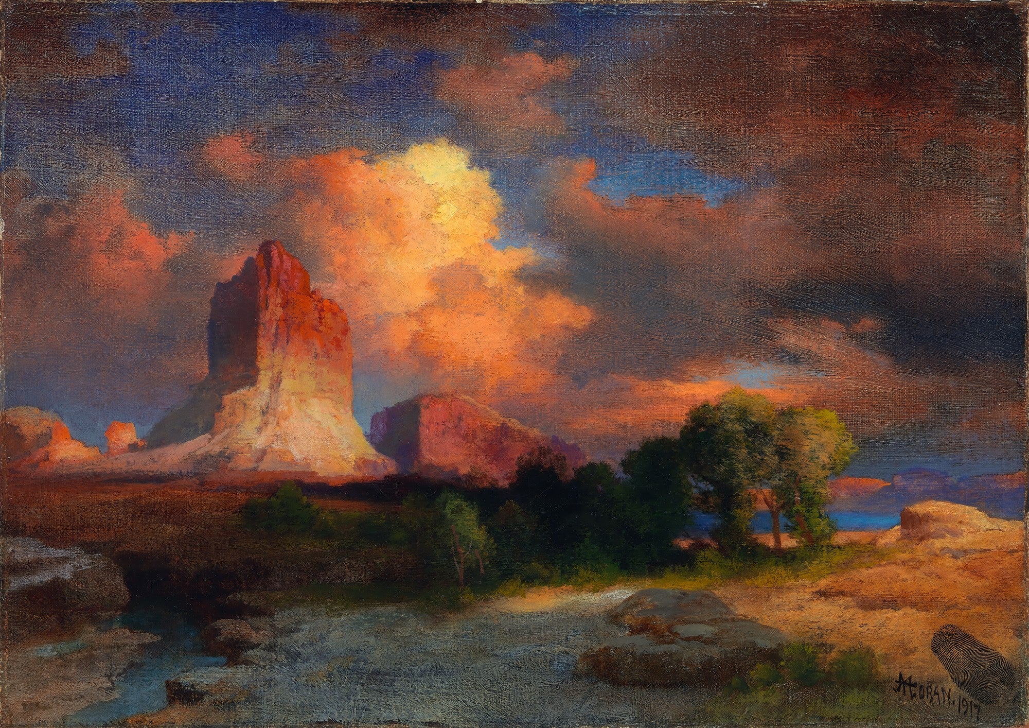 Quadro decorativo com paisagem desértica ao pôr do sol de Thomas Moran. Rochas imponentes em tons de laranja e marrom sob um céu dramático com nuvens em tons de fogo e azul escuro. Vegetação esparsa e um riacho serpenteando em primeiro plano.