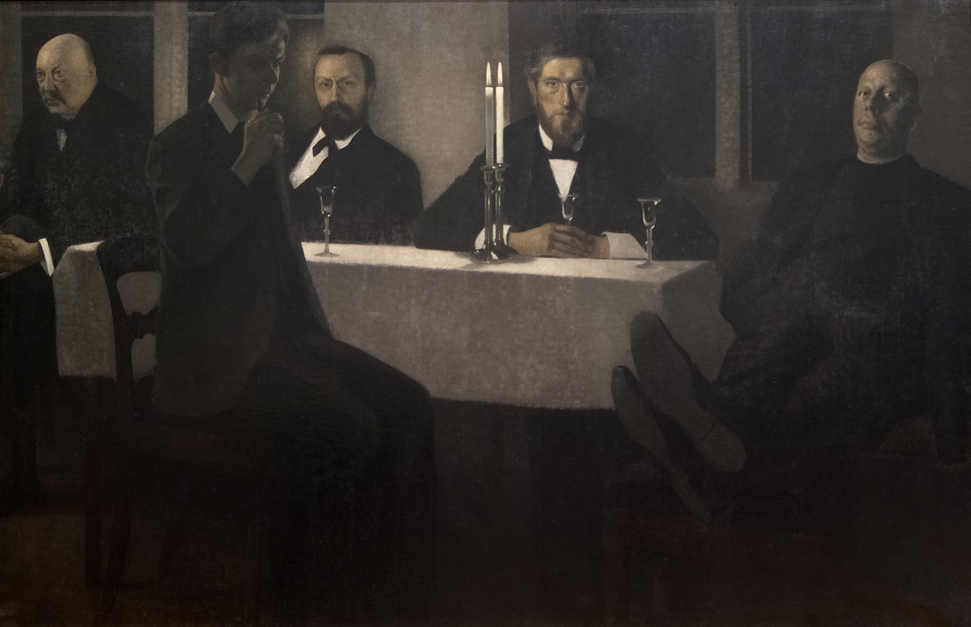 Quadro decorativo com a pintura 'A Grande Reunião' de Vilhelm Hammershøi, mostrando cinco homens em uma mesa escura, com luz suave iluminando alguns rostos e uma vela. Predominam tons de cinza e preto.