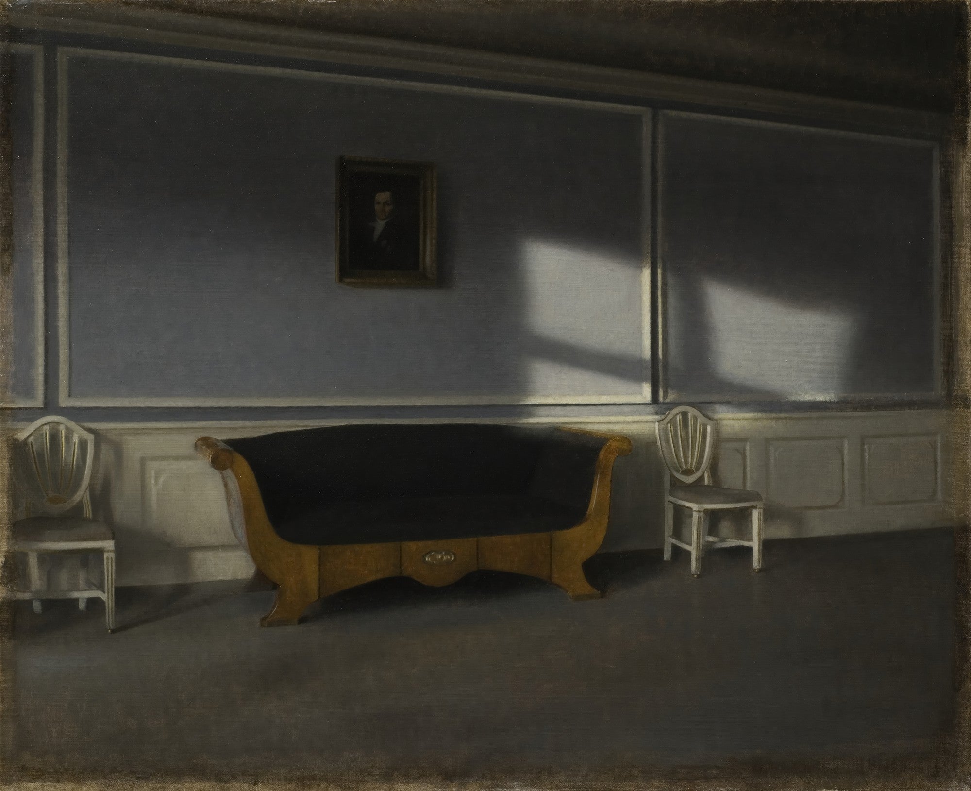 Quadro decorativo mostrando um interior escuro e silencioso de Vilhelm Hammershøi, com um sofá antigo de madeira e estofamento escuro no centro, duas cadeiras laterais brancas, um retrato na parede azul-acinzentada e raios de sol entrando por uma janela invisível, criando padrões de luz e sombra no chão e na parede.